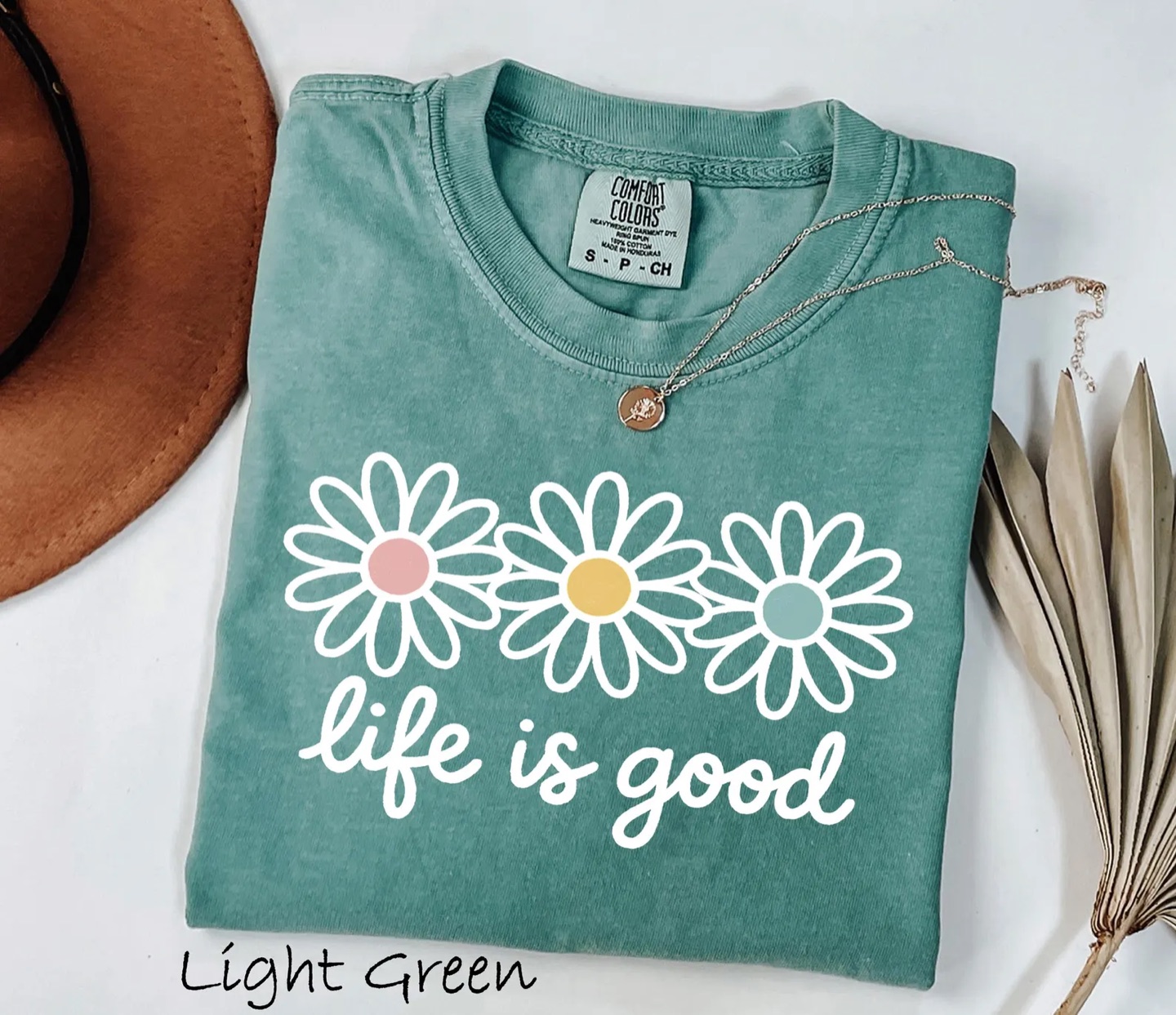 The life is good daisy graphic tee on Comfort Colors, flat lay with straw hat